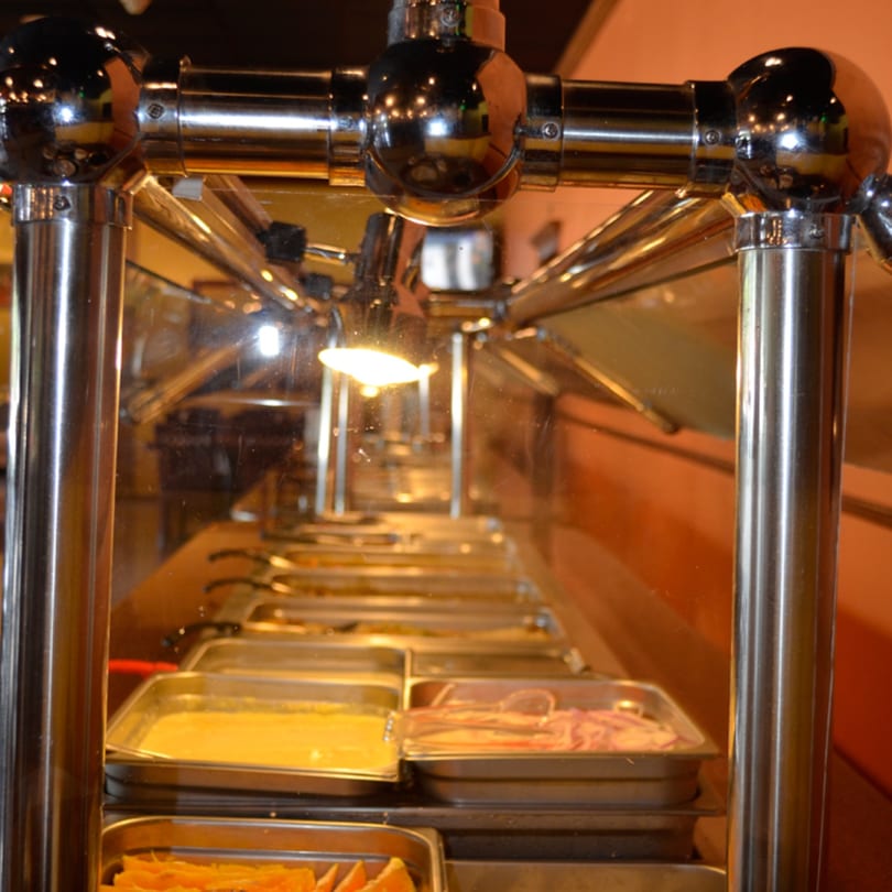 Indian buffet with various dishes in metal trays, illuminated by a warm light.