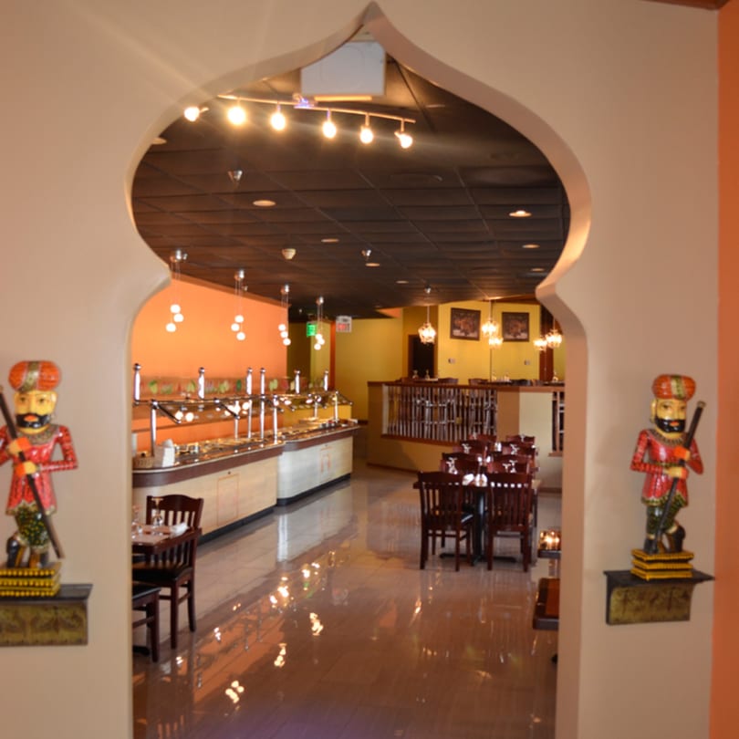Archway entrance to Mint Leaf Indian Cuisine dining area with buffet, tables, and decorative statues.