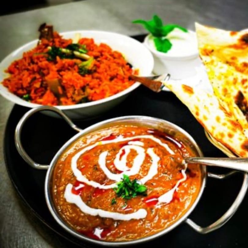 Indian dishes: a bowl of orange curry, a bowl of red rice, and naan bread.