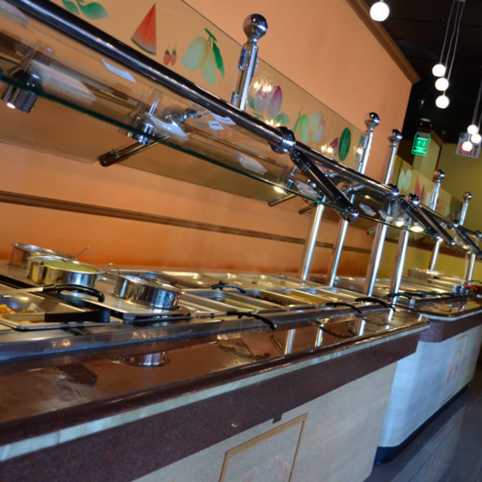 A long, well-lit Indian buffet line with various food pans and serving utensils.
