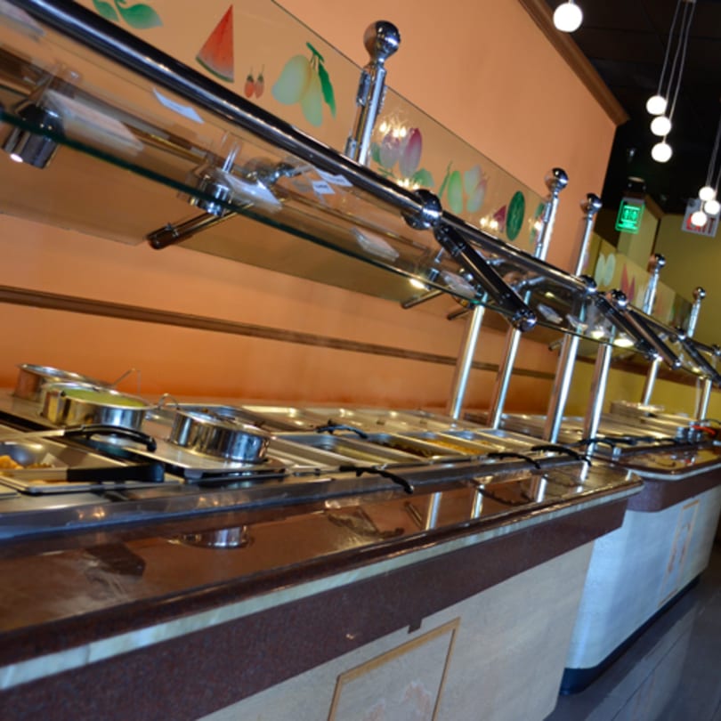 A long, well-lit Indian buffet line with various food pans and serving utensils.