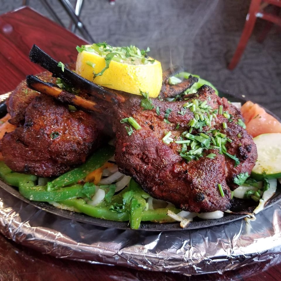 Sizzling Indian lamb chops with green peppers, onions, and a lemon wedge on a hot platter.