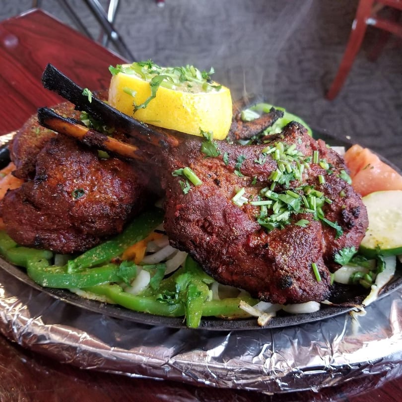 Sizzling Indian lamb chops with green peppers, onions, and a lemon wedge on a hot platter.