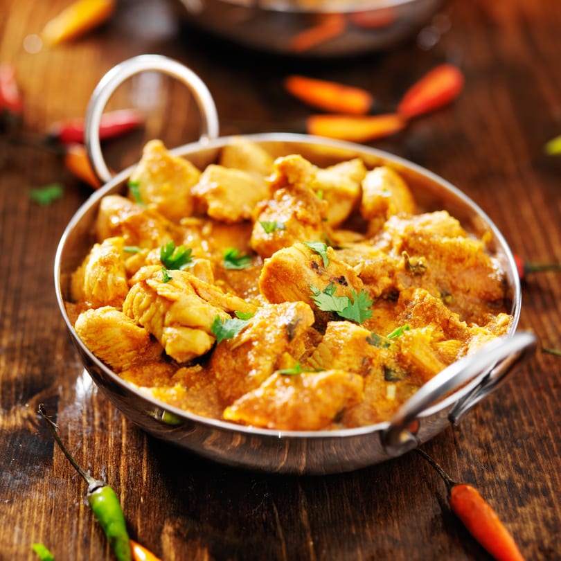 Indian chicken curry in a metal bowl with chili peppers on a wooden table.