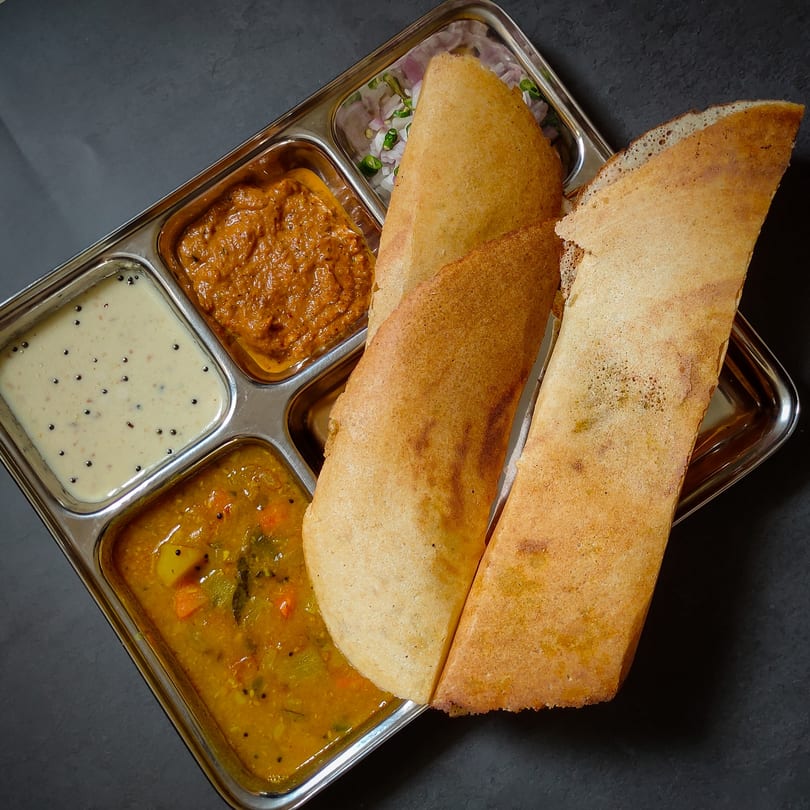 Two golden-brown dosas served with three Indian chutneys and sambar in a steel thali.