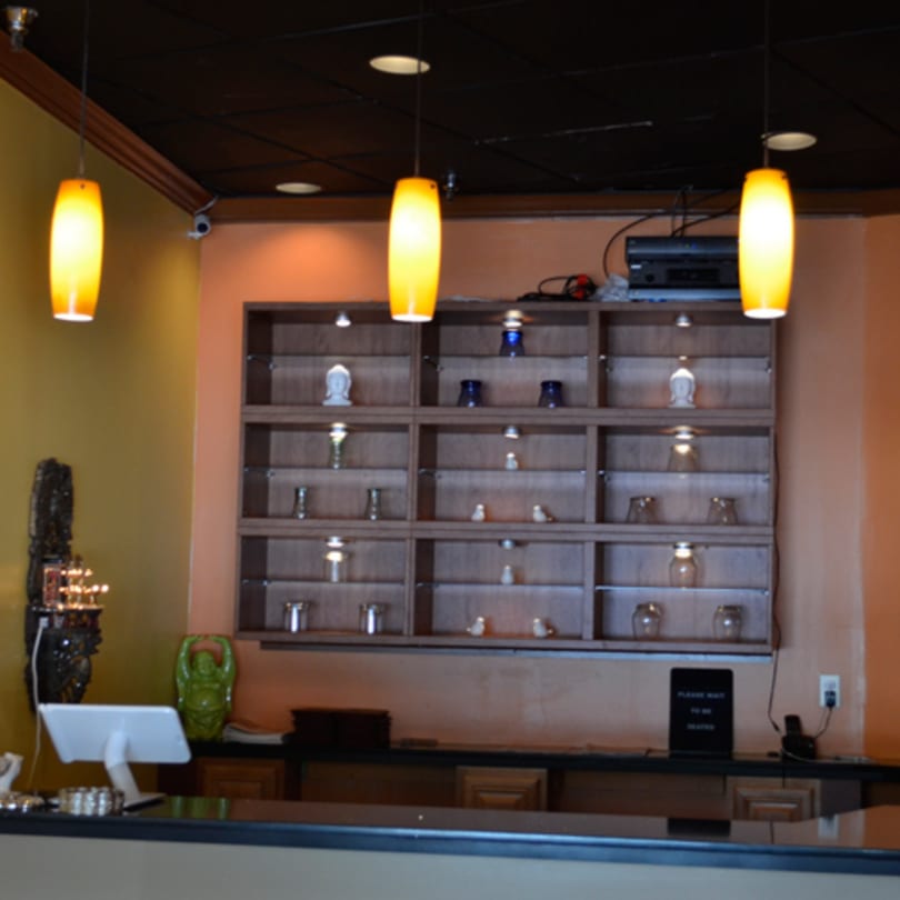 The Mint Leaf Indian Cuisine host stand with a decorative shelf of small statues and glasses.