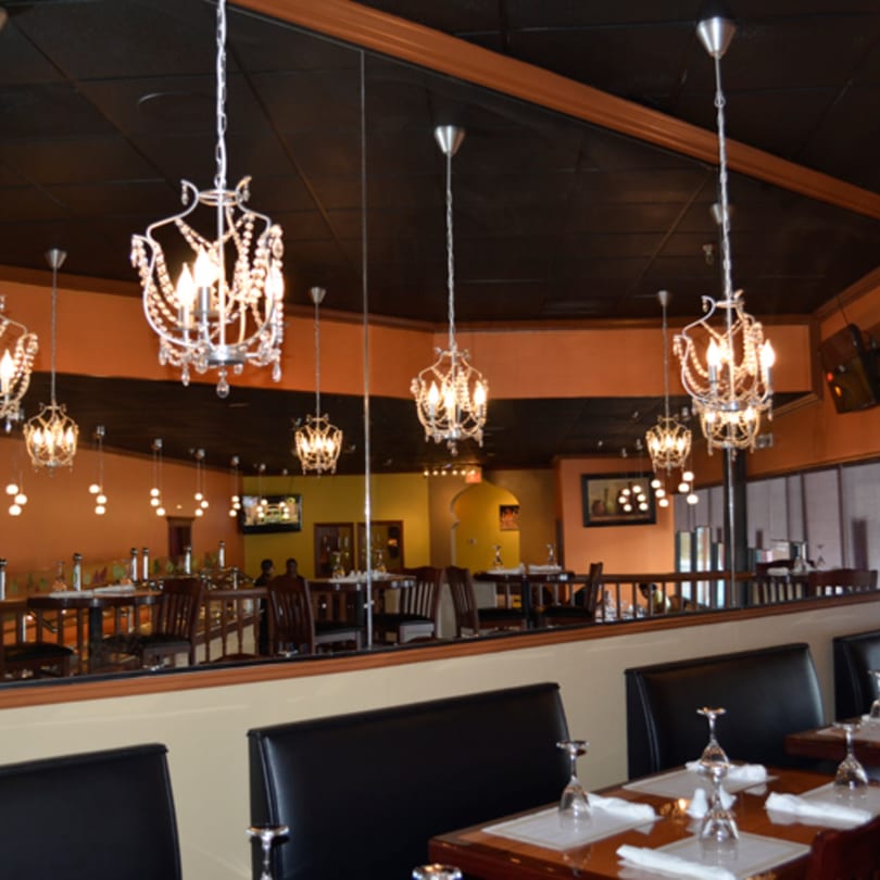 Elegant Indian restaurant interior with chandeliers, black booths, and set tables, reflecting in a large mirror.