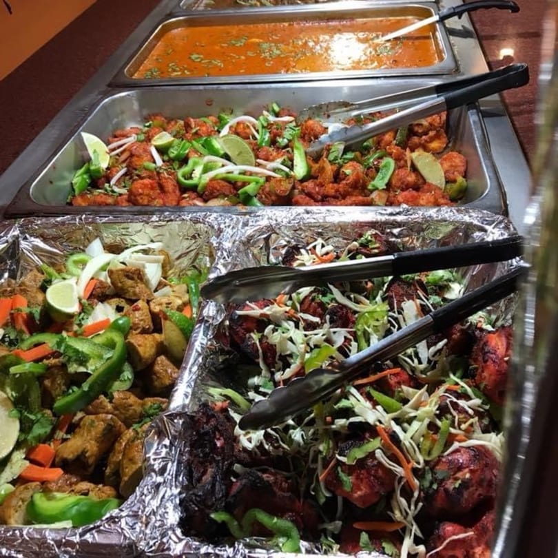 A buffet spread at Mint Leaf Indian Cuisine featuring various Indian dishes in metal trays.
